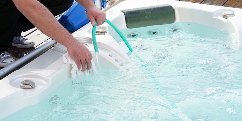 Person cleaning & filling a hot tub - How Can You Maximize the Life of Your Hot Tub Filter Cartridges? 
